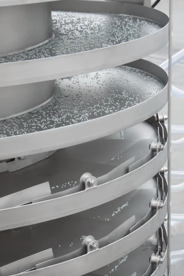 JOEST spiral elevator with bulk material on stainless steel helical conveyor path.