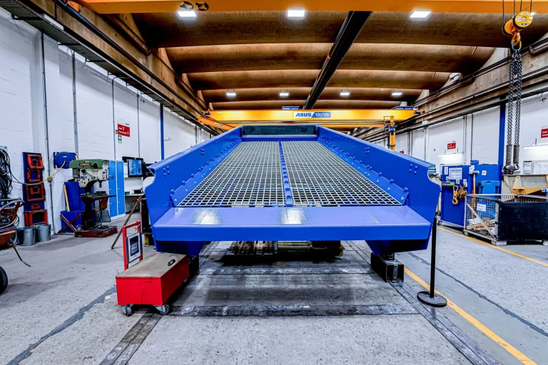 Frontansicht eines blauen JOEST Kreisschwingsiebs mit Gitterdecks in einer Werkhalle.