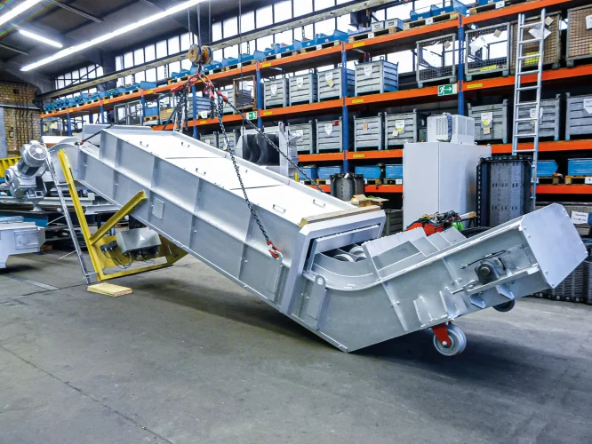Side view of a fully assembled hinged steel plate conveyor in a factory hall