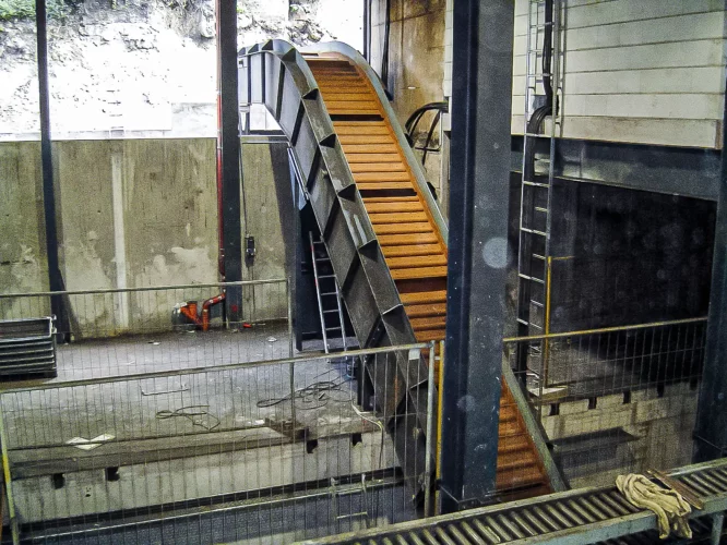 Hinged steel plate conveyor with cleats for vertical material transport in an industrial facility