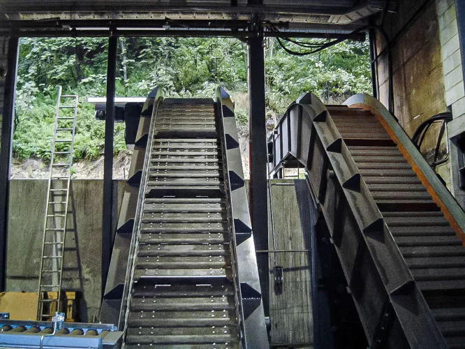 Two hinged steel plate conveyors with cleats for the safe inclined transport of heavy materials in industrial applications