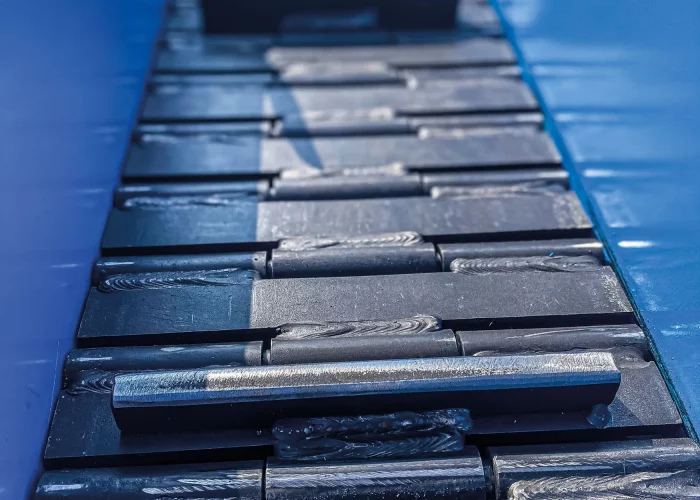 Geschweißte Scharnierglieder mit Mitnehmern auf einem Scharniergurtförderer für den Transport schwerer Werkstücke