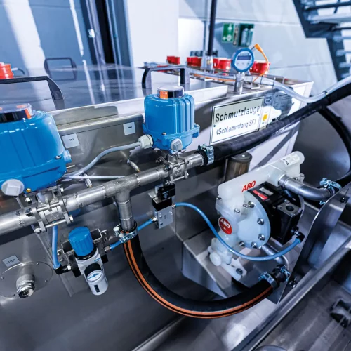 Rohrleitungssystem mit Ventilen, Sensoren und Druckluftpumpe einer industriellen Waschzentrifuge zur Steuerung von Reinigungsflüssigkeit im Metallreinigungsprozess.