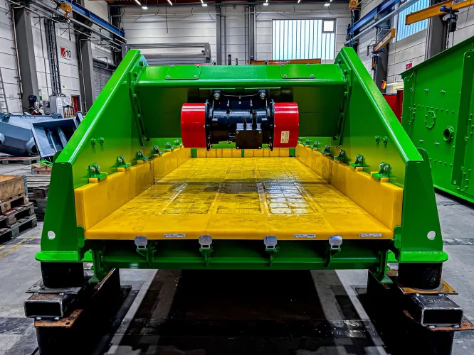 Grünes Entwässerungssieb mit gelber Siebfläche und rotem Vibrationsmotor in einer Werkhalle.